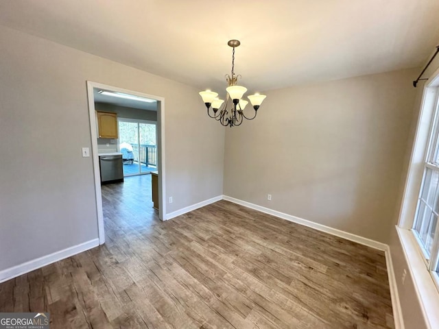 empty room with a chandelier, wood finished floors, and baseboards