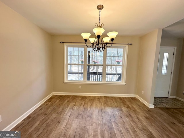 unfurnished dining area featuring dark wood-style floors, a wealth of natural light, a chandelier, and baseboards