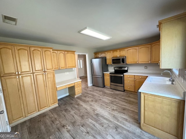 kitchen featuring light wood finished floors, appliances with stainless steel finishes, a sink, and built in desk