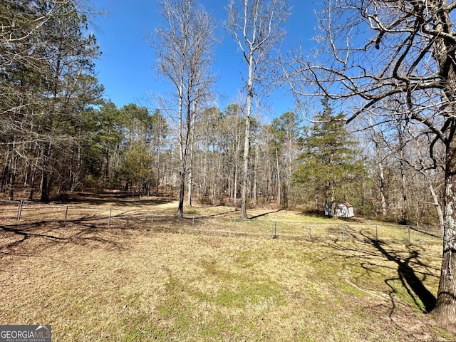 view of yard with a storage shed, fence, a wooded view, and an outbuilding