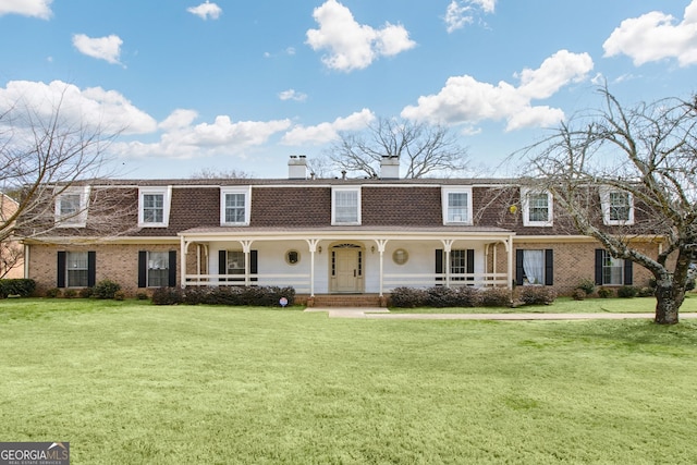 view of front facade with a porch, a front lawn, a chimney, and brick siding