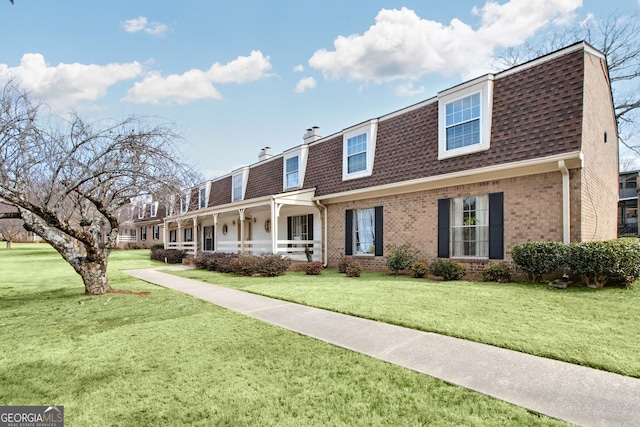 view of front facade featuring roof with shingles, a front yard, a chimney, and brick siding