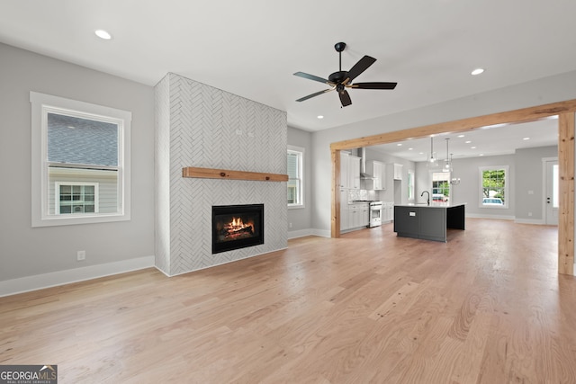 unfurnished living room with baseboards, a ceiling fan, a tiled fireplace, light wood-type flooring, and recessed lighting