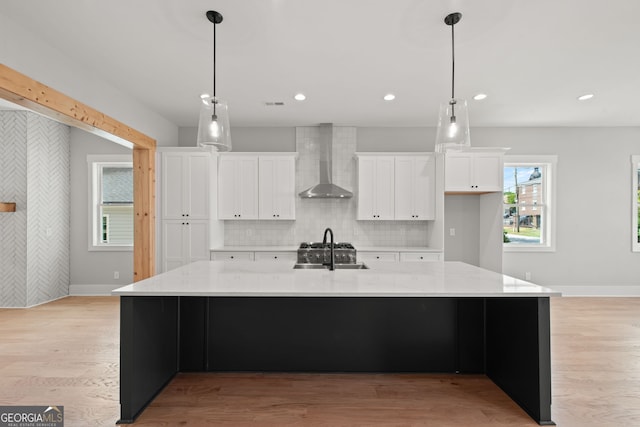 kitchen featuring a large island, white cabinets, a sink, wall chimney range hood, and light wood-type flooring