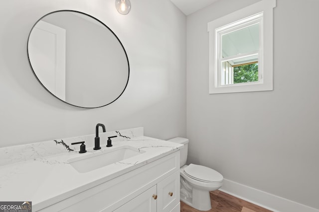 half bathroom featuring baseboards, vanity, toilet, and wood finished floors