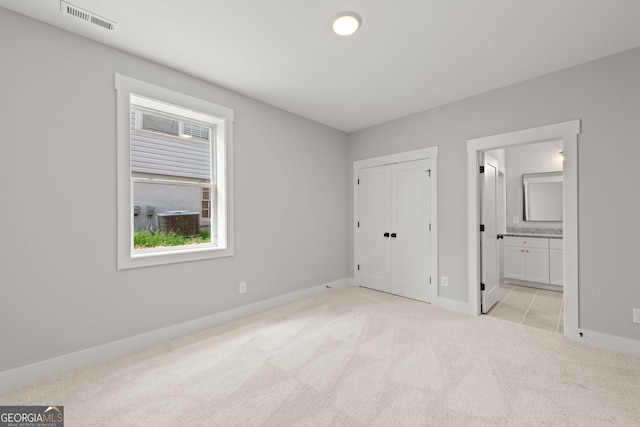 unfurnished bedroom featuring a closet, visible vents, light carpet, ensuite bath, and baseboards