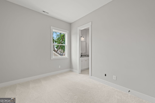 unfurnished bedroom featuring visible vents, light carpet, connected bathroom, a sink, and baseboards