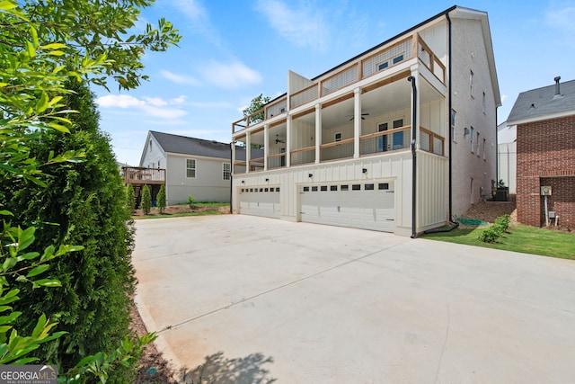 view of front facade with a garage, a ceiling fan, concrete driveway, a balcony, and board and batten siding