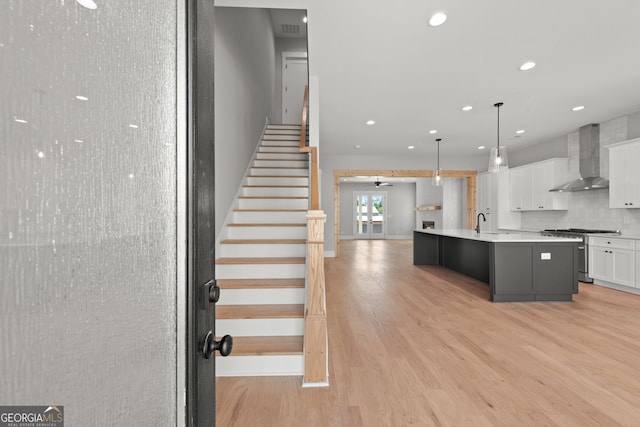 kitchen featuring high end stove, white cabinetry, light wood-style floors, decorative backsplash, and wall chimney exhaust hood