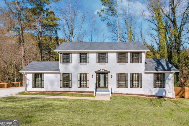 colonial inspired home with a front yard, brick siding, and fence