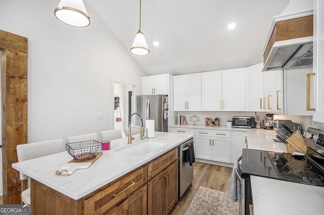 kitchen featuring wood finished floors, appliances with stainless steel finishes, white cabinets, a sink, and light stone countertops