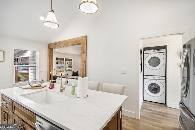 kitchen with decorative light fixtures, appliances with stainless steel finishes, stacked washer / dryer, a sink, and light wood-type flooring