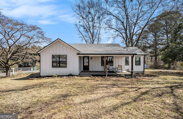 view of front of property featuring board and batten siding, covered porch, fence, and a front lawn