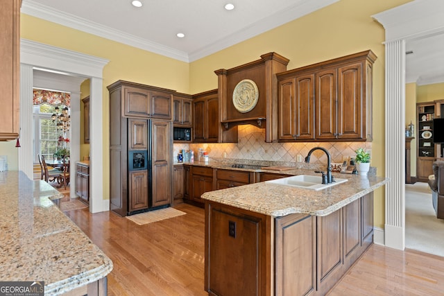 kitchen featuring light stone counters, a peninsula, a sink, backsplash, and light wood finished floors