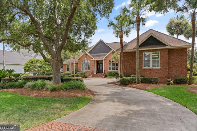 view of front of home featuring driveway, a front yard, and brick siding