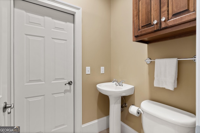 half bath featuring toilet, baseboards, and a sink