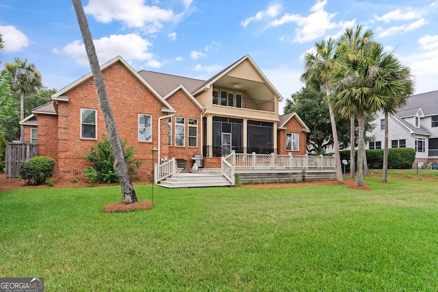 rear view of property with a sunroom, a wooden deck, a lawn, and brick siding