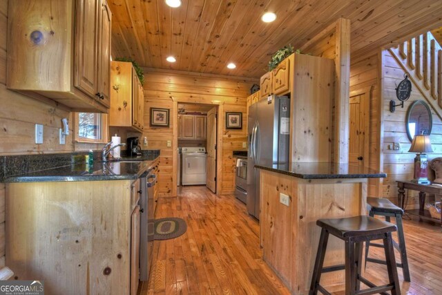 kitchen featuring a breakfast bar area, stainless steel appliances, wood ceiling, wooden walls, and washer / dryer