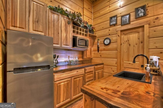 kitchen with stainless steel appliances, a sink, wood counters, and wooden walls