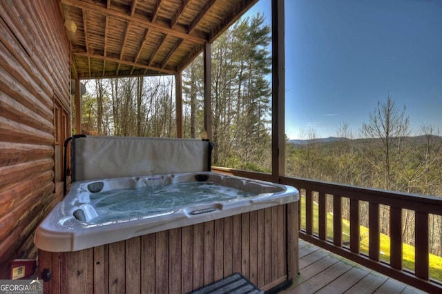 wooden terrace featuring a forest view and a hot tub