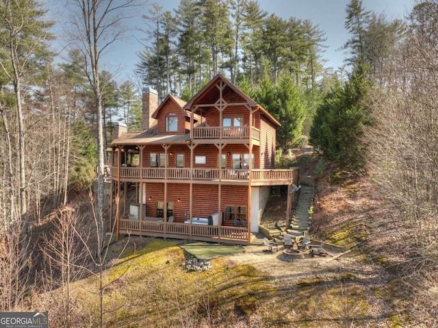 back of property with faux log siding, a balcony, a chimney, stairs, and a deck