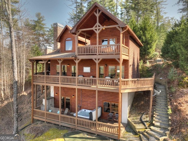 view of front of house featuring faux log siding, a chimney, and a balcony