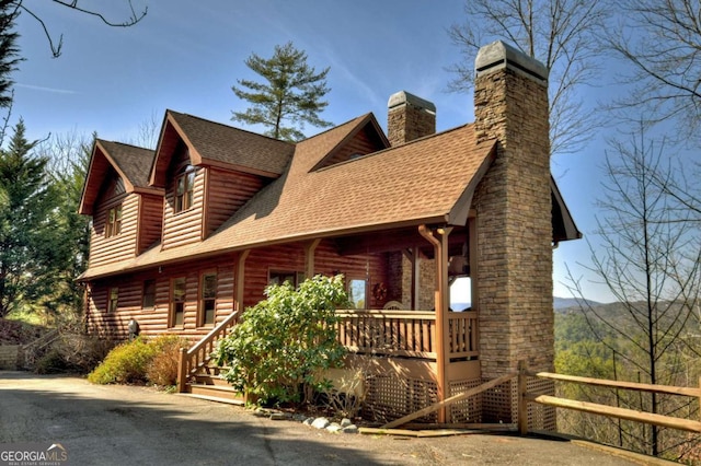 log cabin with covered porch, a chimney, and roof with shingles