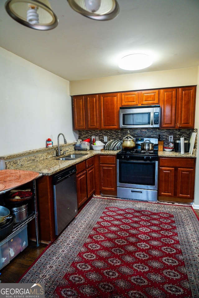 kitchen with appliances with stainless steel finishes, a sink, light stone countertops, and decorative backsplash