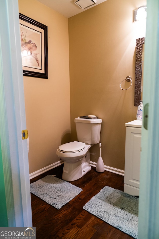 half bathroom with toilet, vanity, baseboards, and wood finished floors