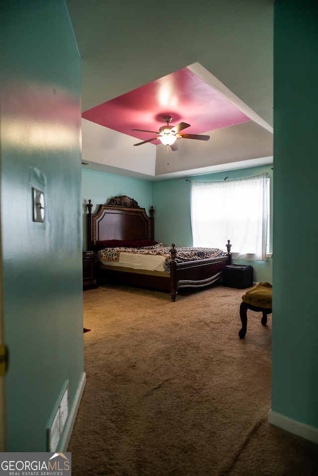 bedroom with a tray ceiling, visible vents, a ceiling fan, carpet flooring, and baseboards