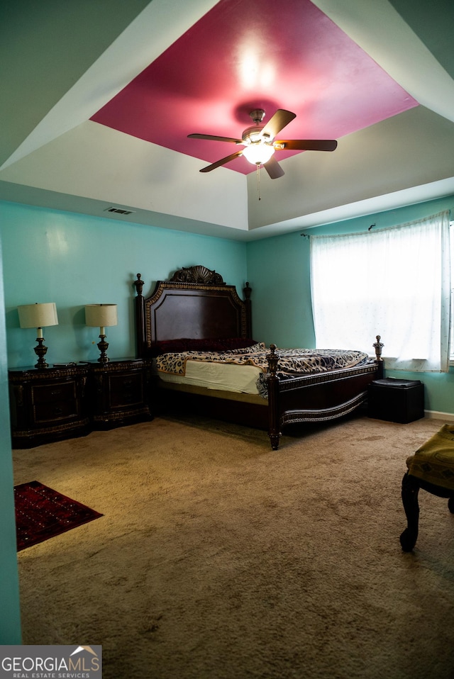 carpeted bedroom with a raised ceiling, visible vents, and ceiling fan