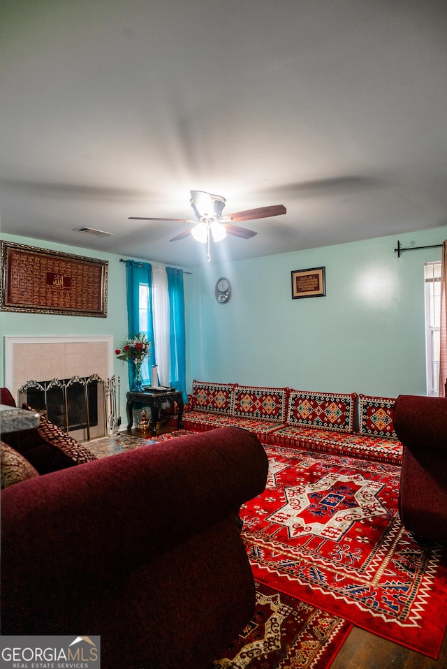 living area featuring ceiling fan, wood finished floors, a tile fireplace, and visible vents