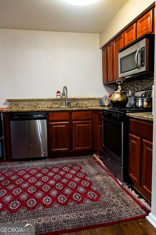 kitchen with stone counters, stainless steel appliances, a sink, decorative backsplash, and dark wood-style floors