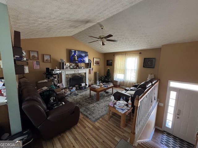 living area featuring lofted ceiling, a fireplace, a textured ceiling, and wood finished floors