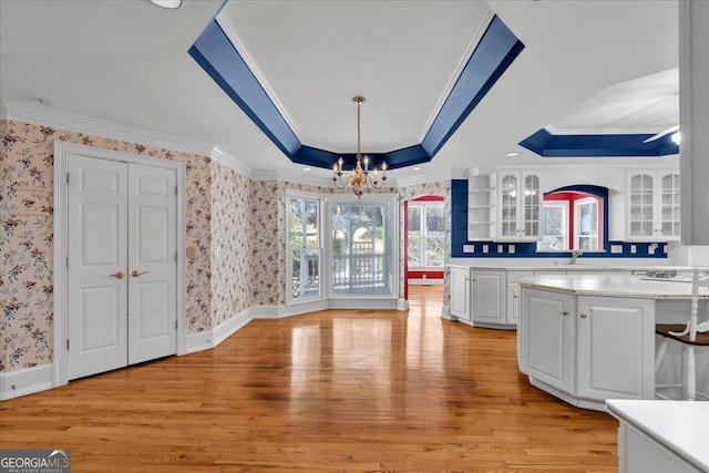 unfurnished dining area with light wood-style flooring, baseboards, wallpapered walls, a tray ceiling, and crown molding