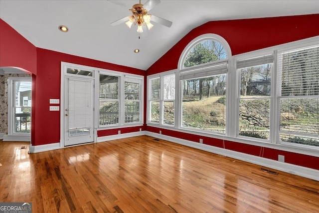 unfurnished sunroom featuring a ceiling fan, arched walkways, vaulted ceiling, and a wealth of natural light