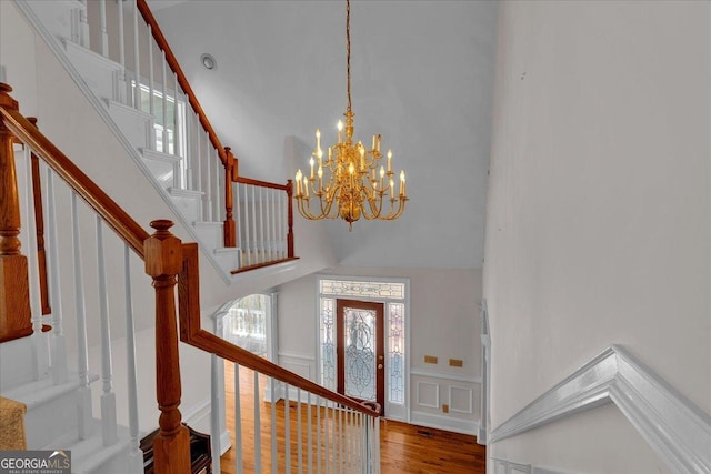 foyer entrance featuring a decorative wall, a high ceiling, wood finished floors, stairs, and wainscoting