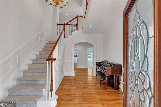 entrance foyer featuring ornamental molding, arched walkways, a decorative wall, and light wood-style flooring