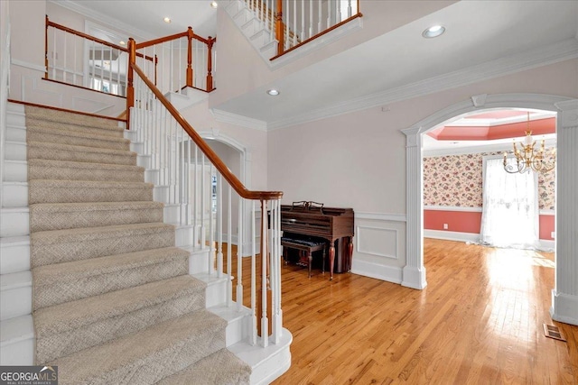 stairway with visible vents, arched walkways, wainscoting, wood finished floors, and crown molding