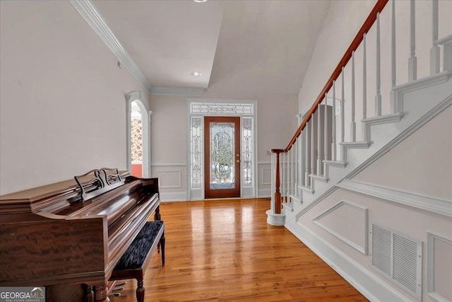 entrance foyer with a decorative wall, wood finished floors, visible vents, stairs, and crown molding