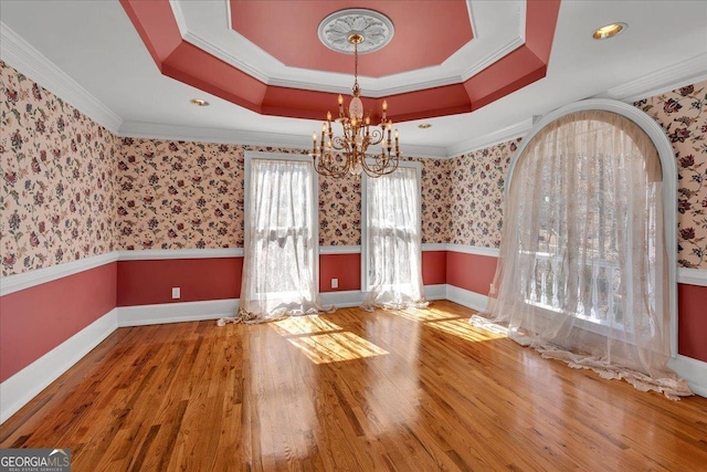 unfurnished dining area with wallpapered walls, arched walkways, wainscoting, wood finished floors, and a tray ceiling