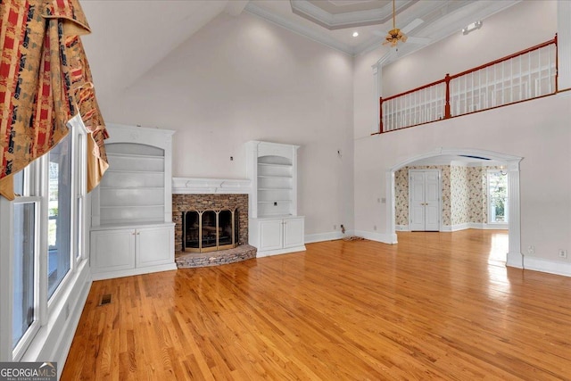 unfurnished living room featuring arched walkways, ornamental molding, a stone fireplace, wood finished floors, and baseboards