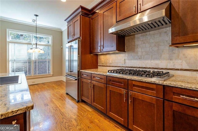 kitchen featuring under cabinet range hood, appliances with stainless steel finishes, light wood finished floors, decorative light fixtures, and crown molding