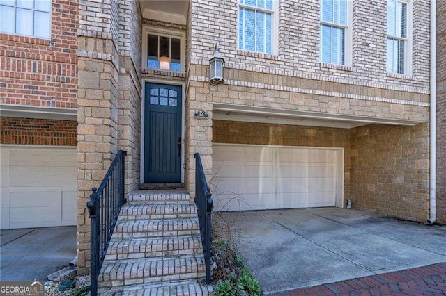 doorway to property featuring driveway, brick siding, and an attached garage