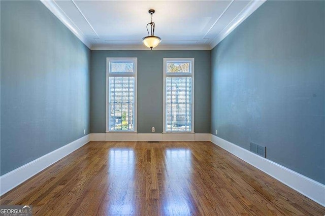 empty room with baseboards, visible vents, wood finished floors, and ornamental molding