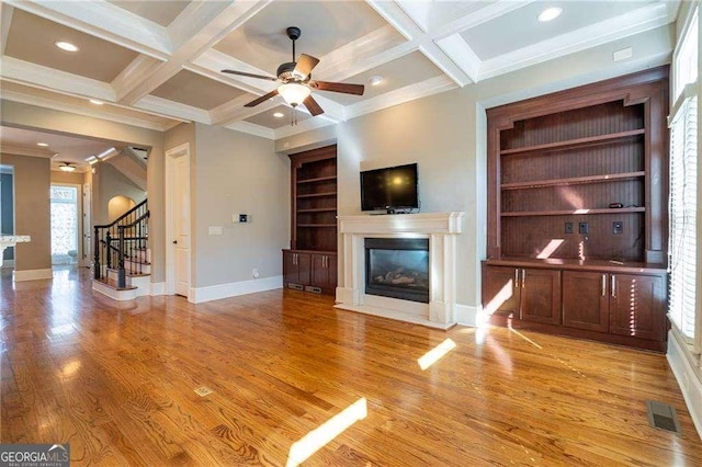 unfurnished living room with light wood-type flooring, stairway, coffered ceiling, and a glass covered fireplace