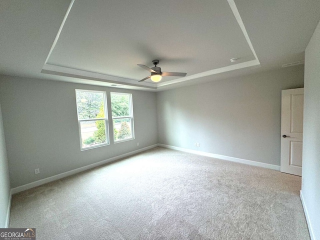 spare room featuring carpet flooring, a raised ceiling, a ceiling fan, and baseboards