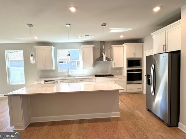 kitchen featuring stainless steel appliances, light wood-style flooring, a kitchen island, wall chimney range hood, and a sink