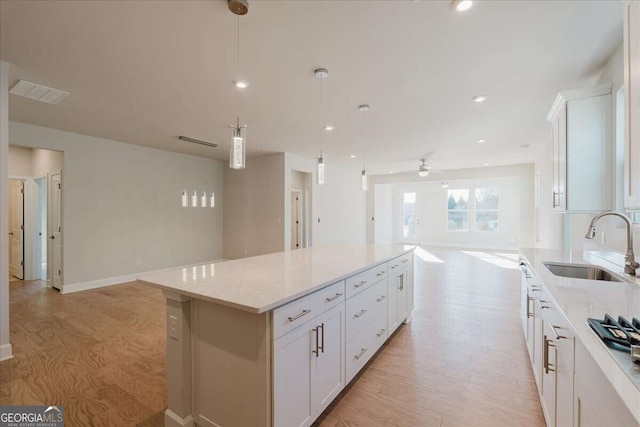 kitchen featuring white cabinets, open floor plan, a center island, light wood-type flooring, and a sink