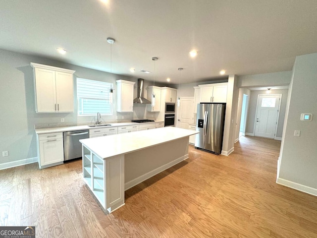 kitchen with a large island, light wood finished floors, stainless steel appliances, white cabinetry, and wall chimney range hood